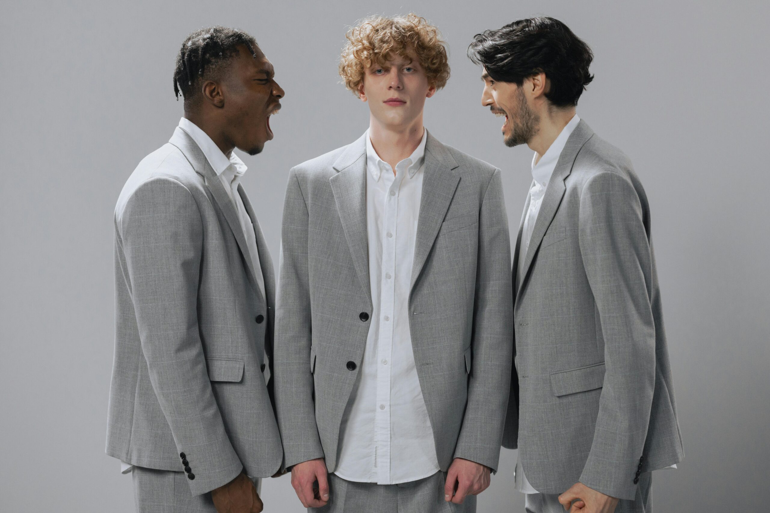 Three men in gray suits demonstrating conflict in a professional setting.